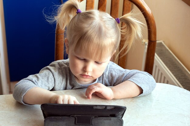 Preschool Caucasian little girl learning online on a digital tablet.