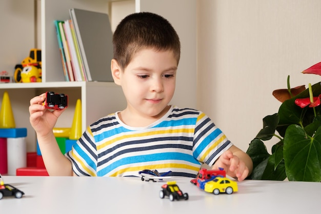 A preschool child plays with toy cars sitting at a table at\
home