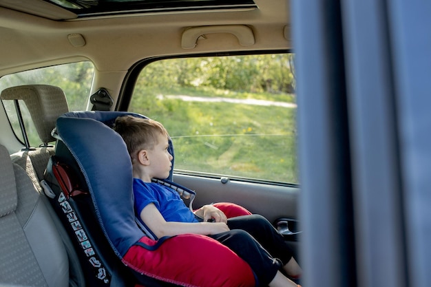 Preschool cute 34 years old boy sitting in safety car seat and crying during family travel by car bad mood negative emotion upbringing and family concept summer outdoor