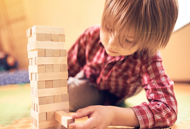 Preschool cute boy playing in a table game with wooden blocks at home