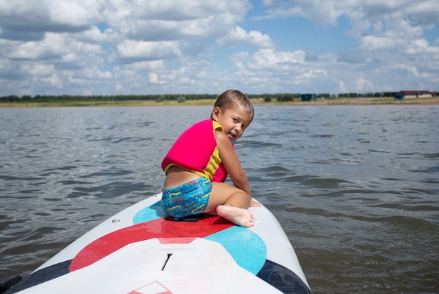 Preschool gelukkige jongen in reddingsvest - jonge surfer leert met plezier op de surfplank te rijden. Actieve gezinslevensstijl, kinderen buiten watersportlessen