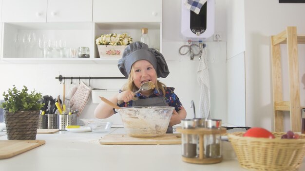 Preschool girl baker mixes the dough in a bowl close up