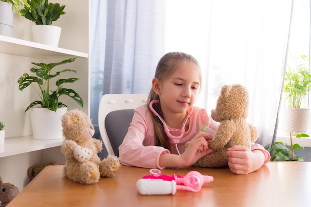 Preschool girl dressed in pink tshirt plays home in hospital with toys puts thermometer toy teddy