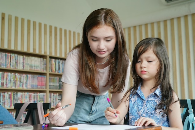 Disegno del bambino della ragazza in età prescolare con la matita di colore su carta bianca sul tavolo in aula con gli amici