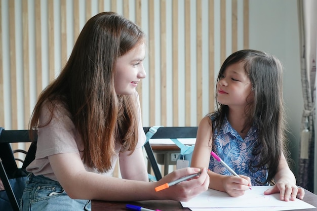 Disegno del bambino della ragazza in età prescolare con la matita di colore su carta bianca sul tavolo in aula con gli amici