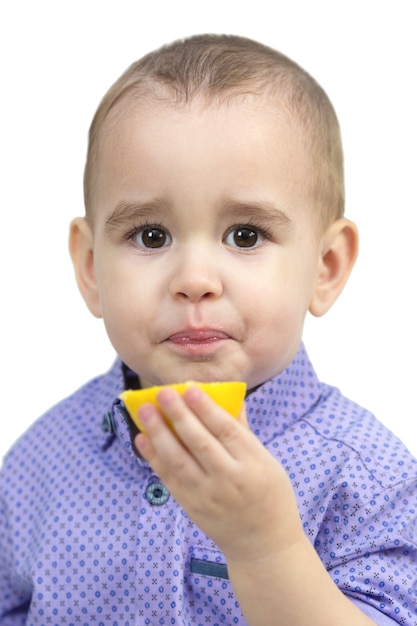 Preschool jongen eten van zure citroen, geïsoleerde witte achtergrond.