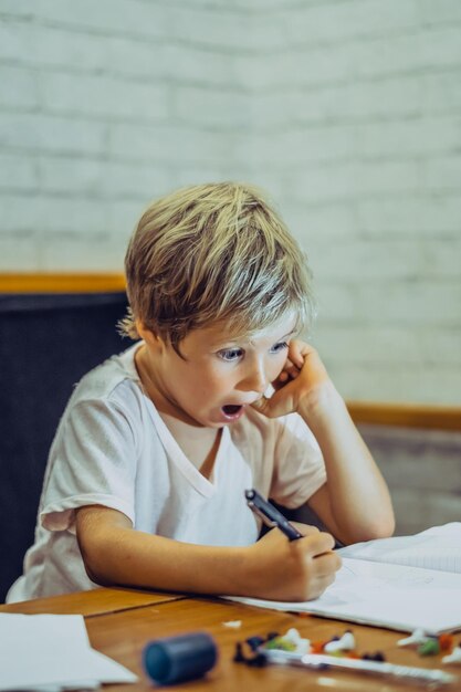 Preschool jongen ondeugende grappige blik verrast open mond ogen houden kin met vinger vasthouden pen notebook schrijven tekenen emotie gezichtsuitdrukkingen gebaren Home onderwijs ontwikkelen verbeelding concept