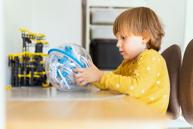 Preschool jongen zit aan de tafel in een kamer en speelt een doolhofspel met obstakels. kind leren thuis. vroege scholing. slimme jongen.