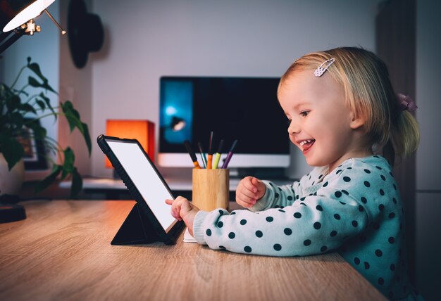 Photo preschool little girl with tablet pc at in evening at home