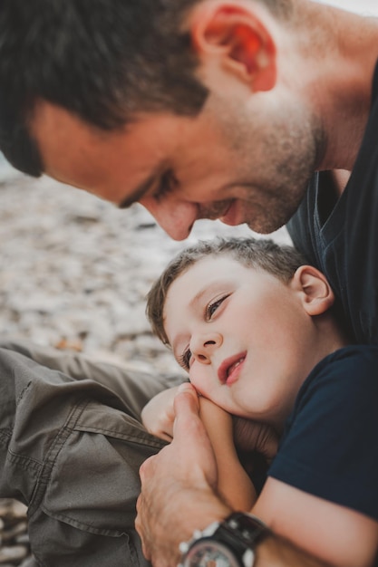 Preschooler boy in a dark blue t-shirt lies in his fathers arms and look away