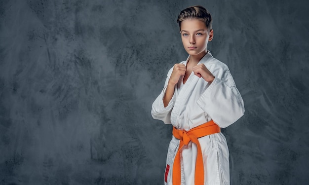 Мальчик-дошкольник, одетый в белое кимоно для карате с оранжевым поясом.