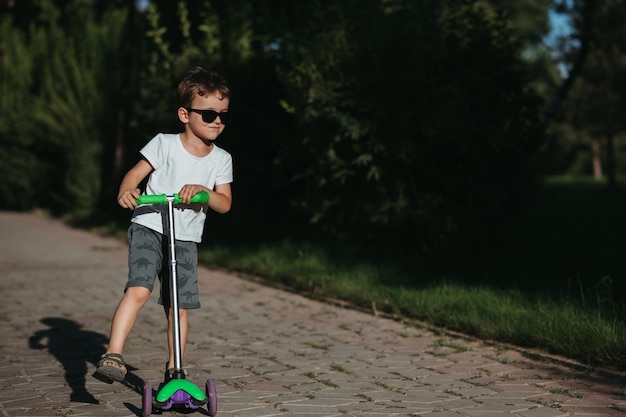preschooler boy rides a scooter in the park in the summer