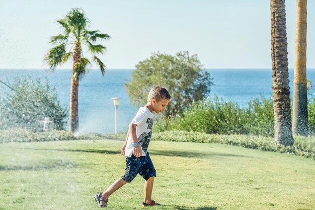 Preschooler boy wet through runs away from watering system on sunny day