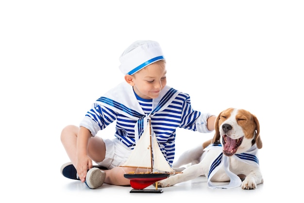 Photo preschooler child in sailor suit with toy ship and beagle dog on white