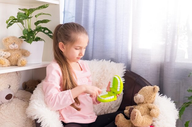 preschooler dressed in pink tshirt plays doctor at home and shows teddy bear how to brush his teeth