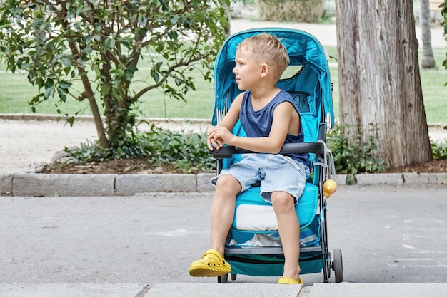 Preschooler frowns sitting in blue stroller of baby brother walking in park