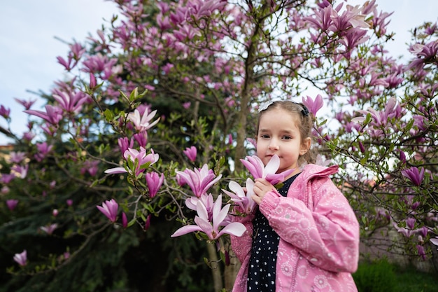 Preschooler girl in pink jacket enjoying nice spring day near magnolia blooming tree Springtime activities