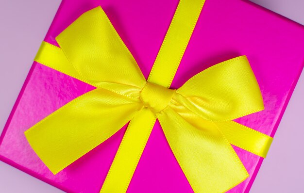 Present box with yellow bow on pink background. Birthday parties. Sale and discount. Christmas shopping ideas. Special offer. Copy space. Black Friday concept.