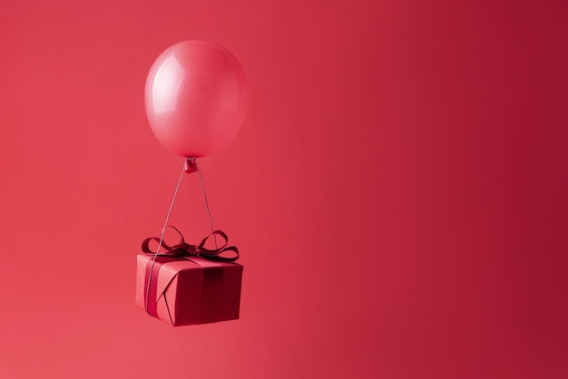 Present flying on a balloon on a red background, gift giving, Valentine's Day and birthday concept.