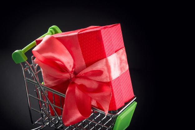 Present gift box in festive packaging with satin bow in the shopping basket.