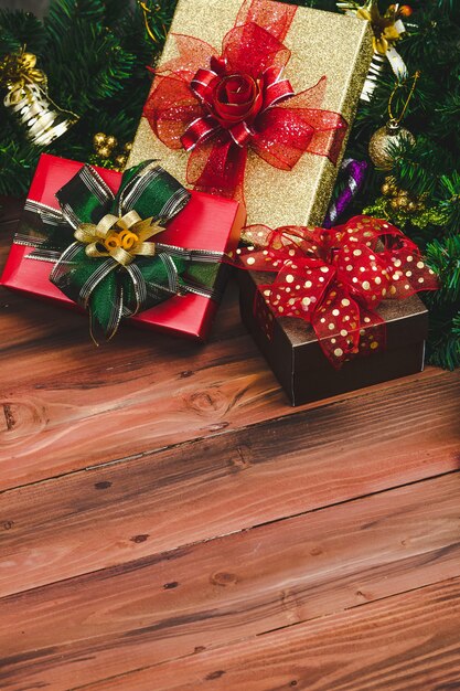 Present gift boxes with colorful ribbon on wood background with Christmas tree and traditional ornaments Xmas props with copy space. Concept of happy and joyful in festival.