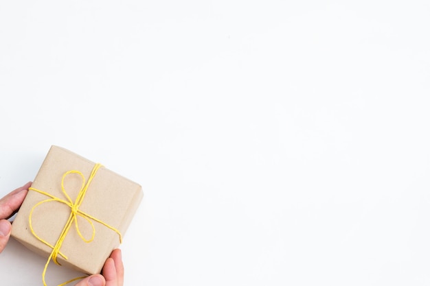 Present wrapped in a craft paper tied with a yellow twine celebratory gift hand offering a simple reward on festive holiday package on white background with copy space