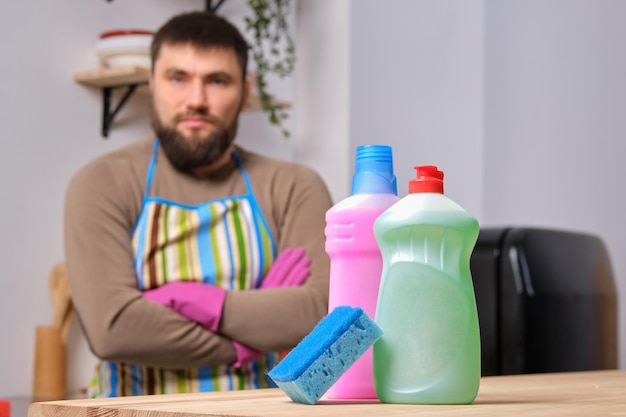 Presentazione di diversi detersivi con asciugamano in primo piano, l'uomo barbuto caucasico è in piedi sullo sfondo con le braccia incrociate