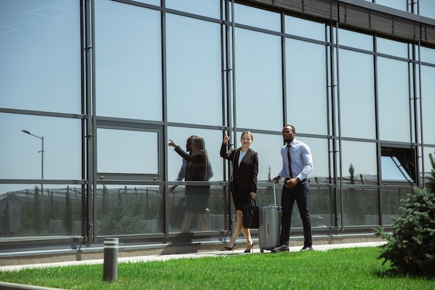 Presentation. Meeting of young business partners after arriving to end point of business trip. Man and woman walking against glass wall background of modern building. Concept of business, finance, ad.