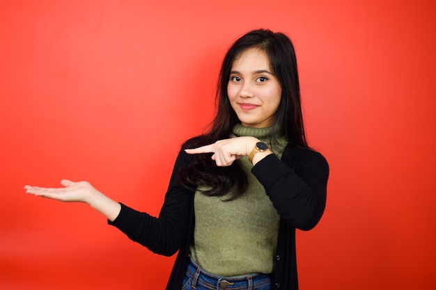 Presentation and pointing product of Young beautiful asian women using black sweater isolated on red