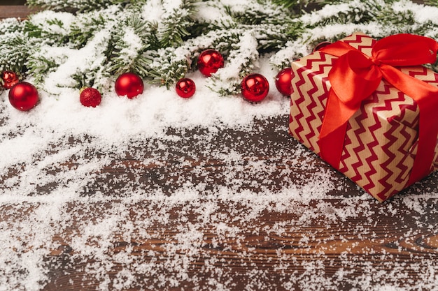 Presenteert op houten met dennenboomtakken en rode kerstballen gepoederd met sneeuw