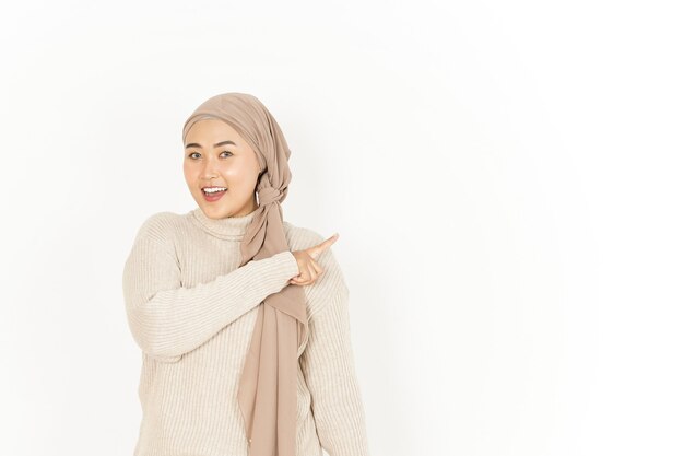 Presentando e indicando da parte della bella donna asiatica che indossa l'hijab isolato su sfondo bianco