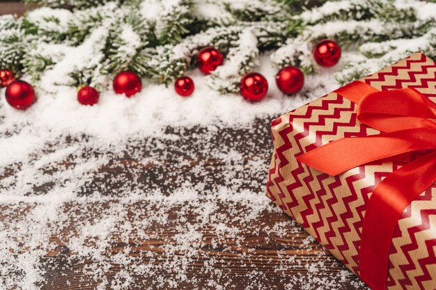 Presents on wooden background with fir tree branches and red baubles powdered with snow