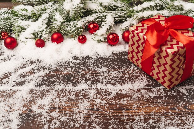 Presents on wooden  with fir tree branches and red baubles powdered with snow