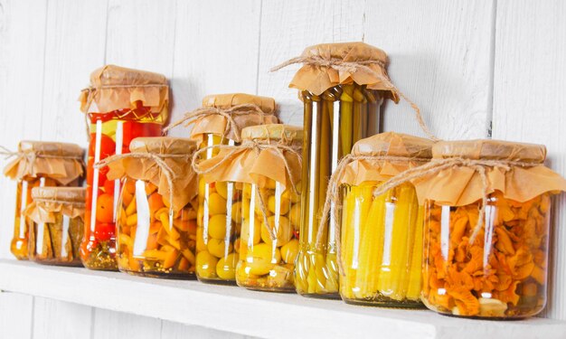 Preserved food in glass jars, on wooden shelf. Various marinaded food