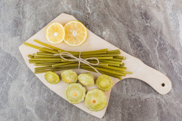 Preserved pattypan squash and sticks next to sliced lemon on a cutting board, on the marble.