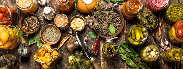 Preserved vegetables in glass jars with seamer on wooden table.