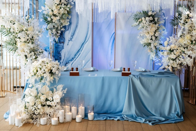 The presidium of the newlyweds in the banquet hall of the restaurant is decorated with candles and green plants, wisteria hangs from the ceiling