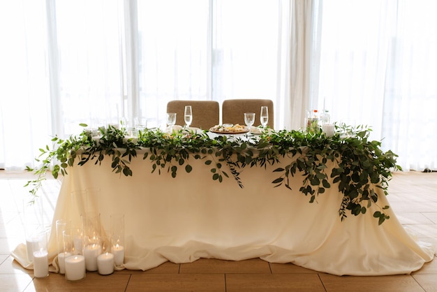 The presidium of the newlyweds in the banquet hall of the restaurant is decorated with candles and green plants wisteria hangs from the ceiling