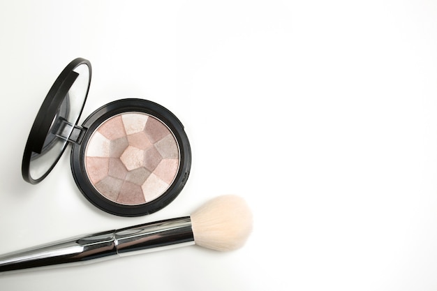 Pressed highlighter with makeup brush over a white background