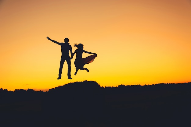 Pret houdend van paar die bij zonsondergang, silhouet springen