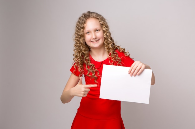 preteen blond meisje wijst met haar vinger naar een blanco vel papier