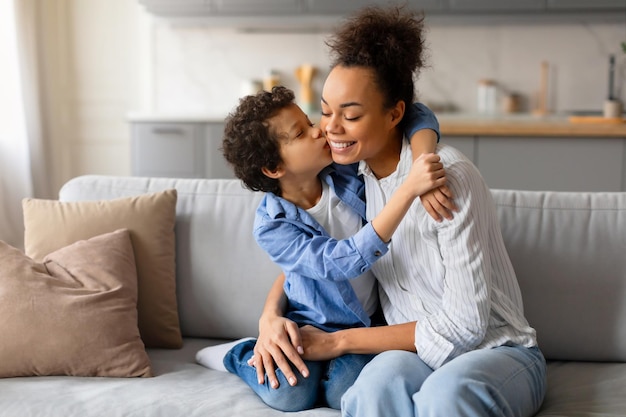 Photo preteen boy gives loving kiss on the cheek to his joyful mother