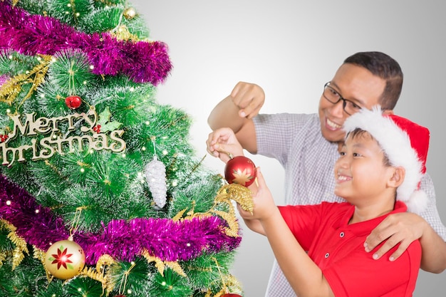 Preteen boy helped by his father decorate a fir tree