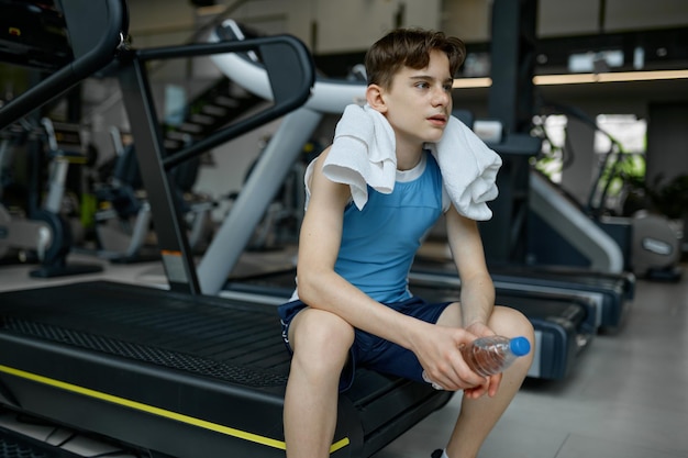 Preteen boy rest after hard training workout on treadmill at gym