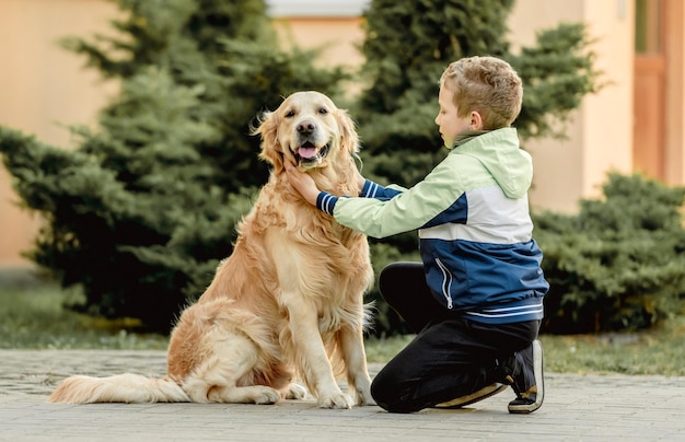 Preteen boy with golden retriever dog sitting outdoors Child kid with doggy pet at street