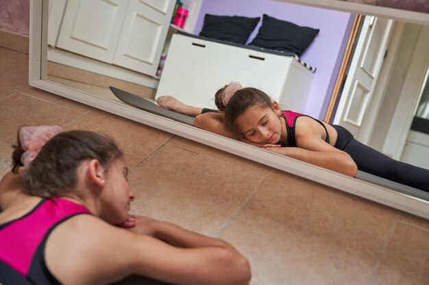 Preteen flexibel meisje met gesloten ogen rustend op de sportmat en benen in spleten strekken tijdens de training thuis