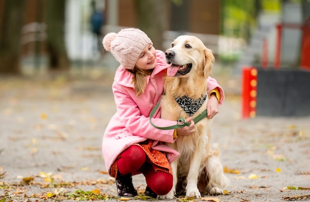 Preteen girl kid with golden retriever dog sitting in the park smiling and petting doggy female chil...