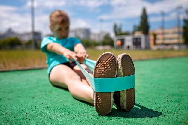 Preteen girl making exercises with fitness resistance band at public sportsground in city sport