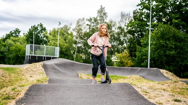 Ragazza preteen che guida scooter nel parco bambina carina con veicolo ecologico all'aperto