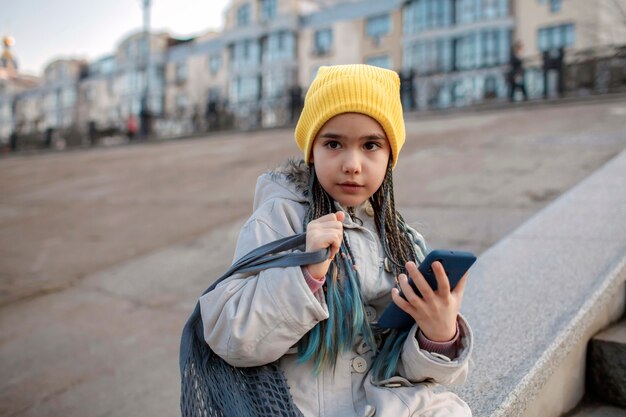 Preteen girl sitting on street stairs and texting with smartphon